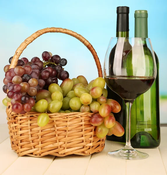 Ripe grapes in wicker basket, bottles and glass of wine, on bright background — Stock Photo, Image