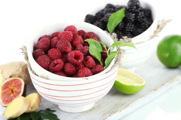 Raspberries and blackberry in small bowls on board isolated on white — Stock Photo, Image