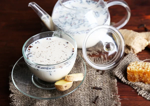 Teapot and cup of tea with milk and spices on sackcloth of wooden table — Stock Photo, Image