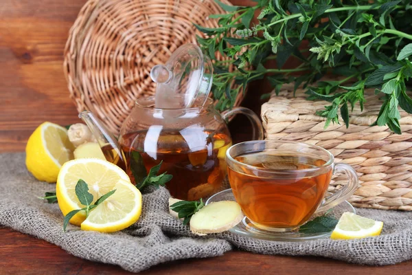 Hervidor de agua y taza de té con jengibre sobre tela de saco sobre mesa de madera sobre fondo brillante —  Fotos de Stock