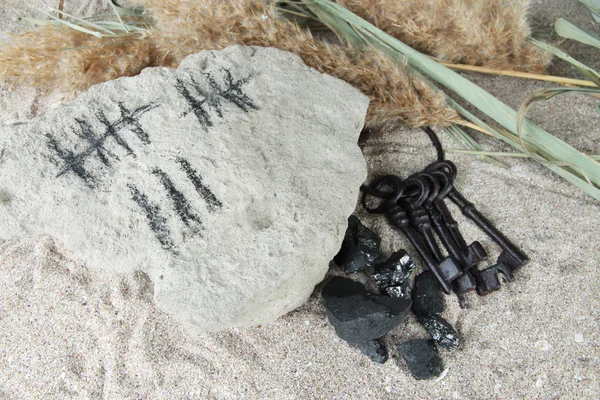 Zählen von Tagen durch Zeichnen von Stöcken auf Stein mit Schlüsseln auf Sandgrund — Stockfoto