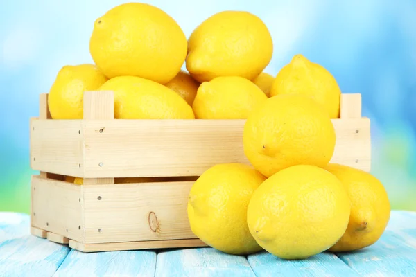 Limoni maturi in scatola di legno sul tavolo su sfondo luminoso — Foto Stock