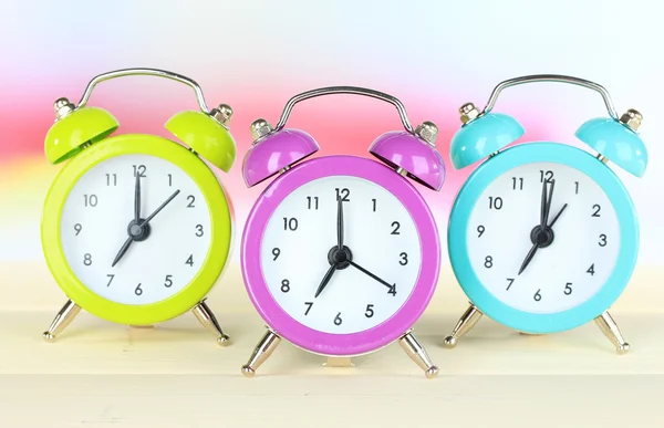 Relógios de alarme coloridos na mesa no fundo claro — Fotografia de Stock
