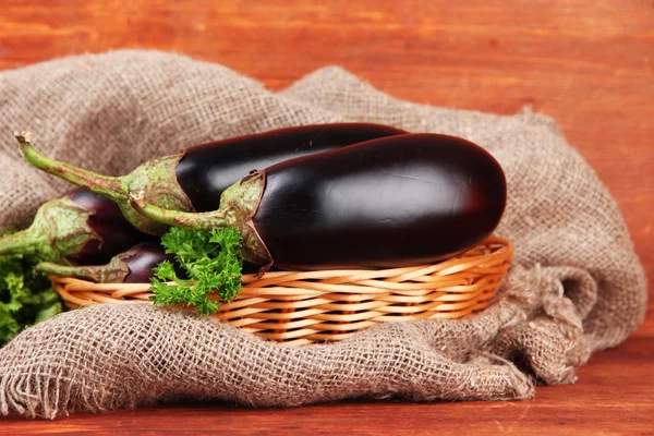 Frische Auberginen im Weidenkorb auf dem Tisch auf Holzgrund — Stockfoto