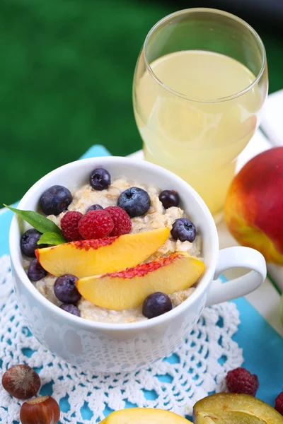 Oatmeal in cup with berries on napkin on table on grass background — Stock Photo, Image