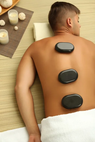 Ung man koppla av med varma stenar på rygg innan massage — Stockfoto