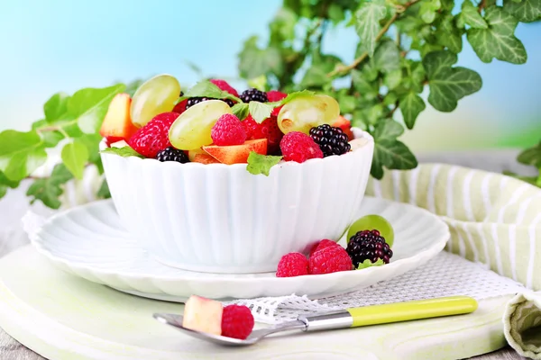 Salada de frutas na tigela, na mesa de madeira, no fundo brilhante — Fotografia de Stock