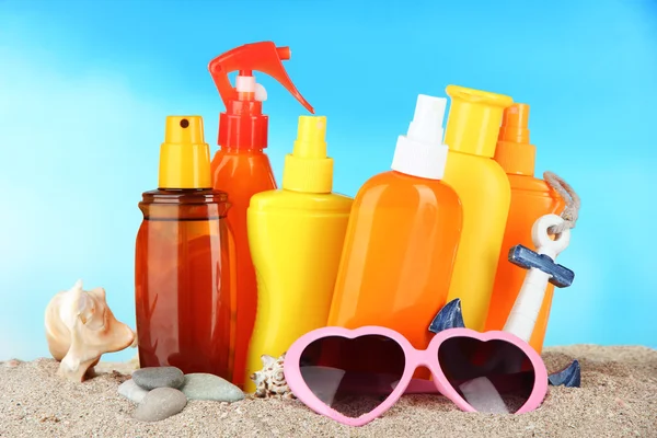 Botellas con crema bronceadora y gafas de sol, sobre fondo azul —  Fotos de Stock