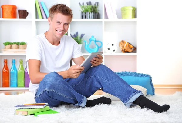 Mladý muž relaxační na koberci s tablet, na pozadí šedé zdi — Stock fotografie