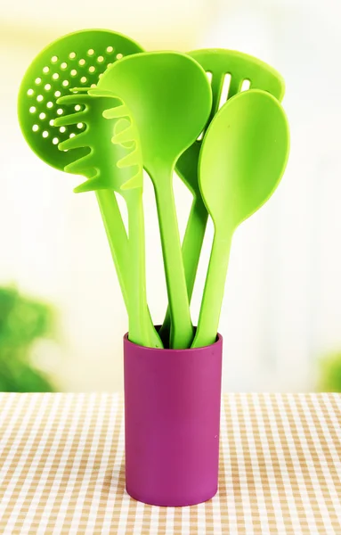 Plastic kitchen utensils in stand on tablecloth on bright background — Stock Photo, Image