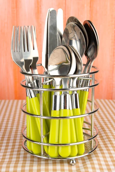 Knives, forks and spoons in metal stand on tablecloth on orange background — Stock Photo, Image