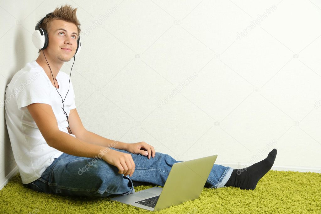 Young man relaxing on carpet and listening to music, on gray wall background