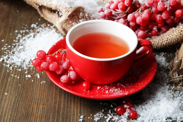 Stilleben med viburnum te i koppen, bär och snö, på säckväv Servett, på trä bakgrund — Stockfoto