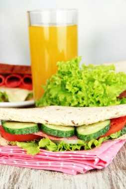 Lezzetli sandviç salam sosis ve parlak zemin üzerine ahşap masa üzerinde renkli peçete üzerinde sebze ve meyve suyu ile kompozisyon