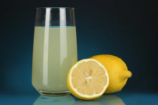 Delicioso zumo de limón en vaso y limones al lado sobre fondo azul oscuro — Foto de Stock