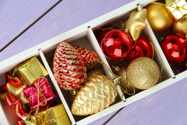 Holzkiste gefüllt mit Weihnachtsschmuck, auf farbigem Holzgrund — Stockfoto