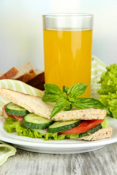 Složení s ovocnou šťávou a chutný sendvič s salám klobása a zeleniny na barevný ubrousek, na dřevěný stůl, na světlé pozadí — Stock fotografie