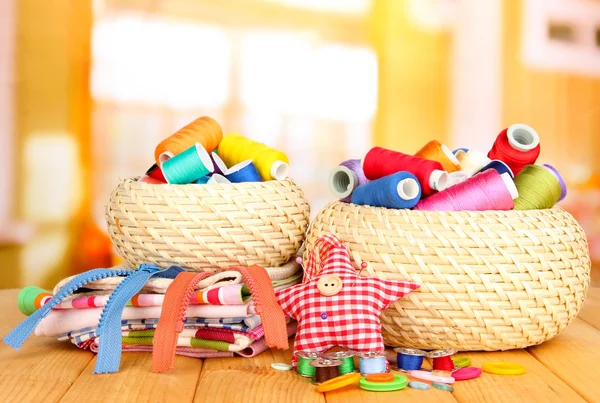 Wicker baskets with accessories for needlework on wooden table, on bright background — Stock Photo, Image