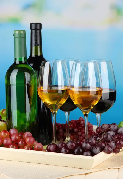 Wine bottles and glasses of wine on tray, on bright background — Stock Photo, Image