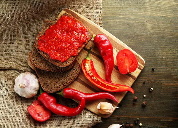 Composition with salsa sauce on bread,, red hot chili peppers and garlic, on sackcloth, on wooden background — Stock Photo, Image