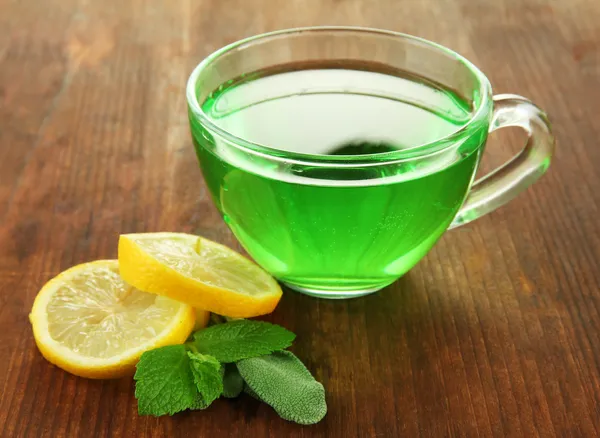 Taza transparente de té verde con limón y menta sobre fondo de madera —  Fotos de Stock