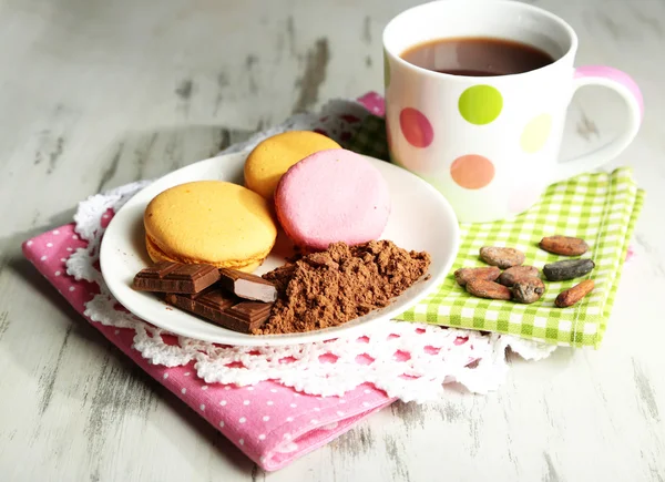 Kakao im Becher mit Süßigkeiten und Kakaopulver auf Teller auf Holztisch — Stockfoto