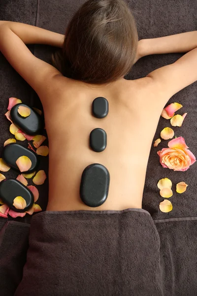 Mooie jonge vrouw met stenen massage in de spa salon over kleur achtergrond — Stockfoto