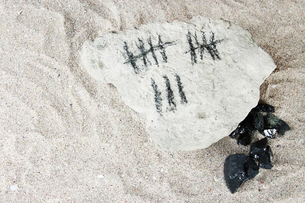 Tage zählen durch Ziehen von Stöcken auf Stein mit Kohle auf Sandgrund — Stockfoto