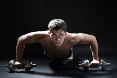 yakışıklı genç kaslı sporcu, koyu arka plan üzerinde egzersiz halter ile yürütmek