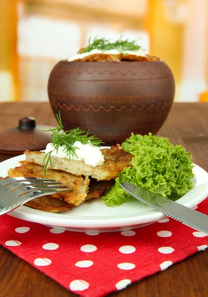 Aardappelpannenkoekjes in pot, op houten tafel, op lichte achtergrond — Stockfoto