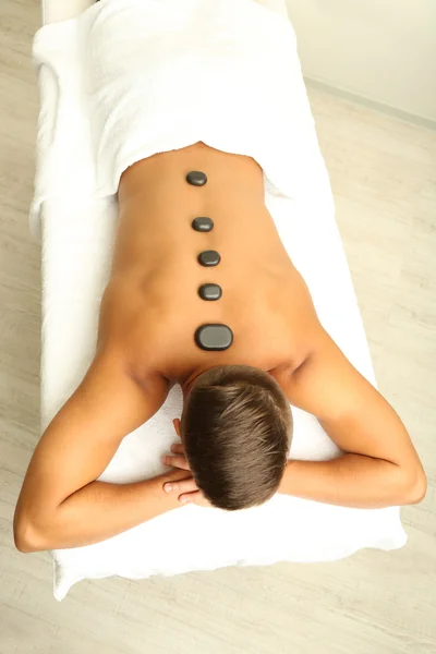 Jovem relaxante com pedras quentes nas costas antes da massagem — Fotografia de Stock