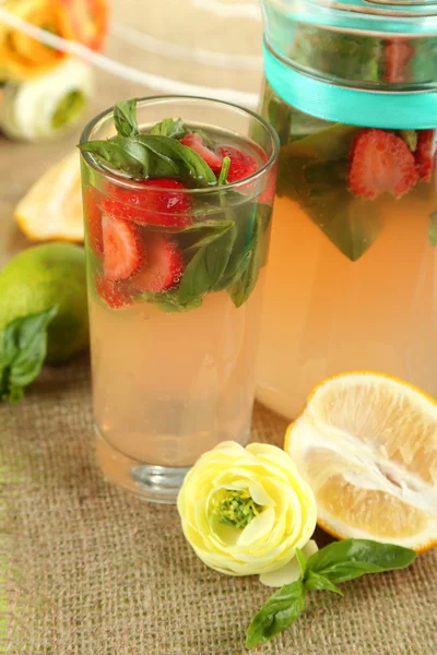 Basil lemonade with strawberry in jug and glass, on wooden table, on bright background — Stock Photo, Image