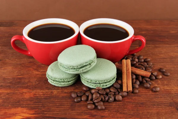 Copos vermelhos de café forte com grãos de café e biscoitos na mesa no fundo marrom — Fotografia de Stock