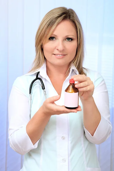 Jonge mooie dokter houden fles geneesmiddel, op lichte achtergrond — Stockfoto