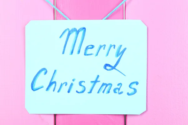 Cartello con le parole Buon Natale su sfondo tavolo in legno rosa primo piano — Foto Stock