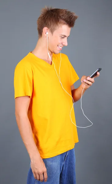 Pohledný mladý muž poslouchat hudbu na šedém pozadí — Stock fotografie