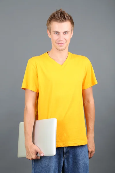 Un joven guapo con portátil sobre fondo gris — Foto de Stock