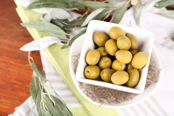 Olive in ciotola con ramo su tovagliolo su tavola di legno — Foto Stock