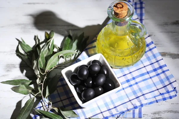 Oliven in Schale mit Zweig auf Sacktuch auf Holzbrett auf Tisch — Stockfoto