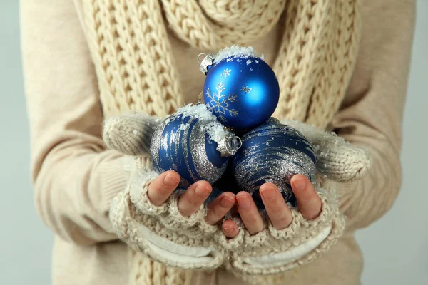 Mãos femininas em mitenes bolas de árvore de Natal, em fundo de cor — Fotografia de Stock