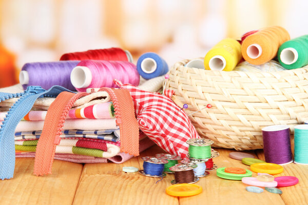 Плетеная корзина с аксессуарами для рукоделия на деревянном столе, на ярком фоне
