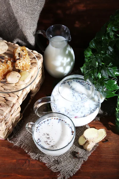 Teiera e tazza di tè con latte e spezie su sacco di tavolo in legno su sfondo luminoso — Foto Stock