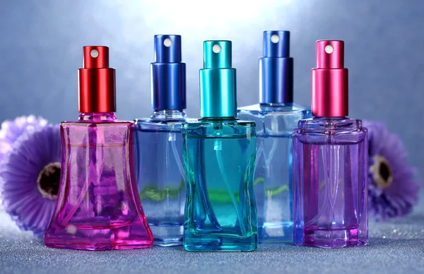 Perfume de mujer en hermosas botellas y flores sobre fondo azul —  Fotos de Stock
