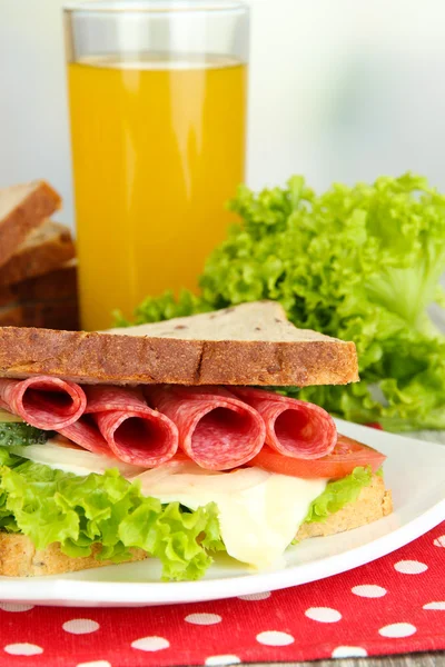 Composição com suco de frutas e sanduíche saboroso com salsicha de salame e legumes em guardanapo de cor, na mesa de madeira, no fundo brilhante — Fotografia de Stock