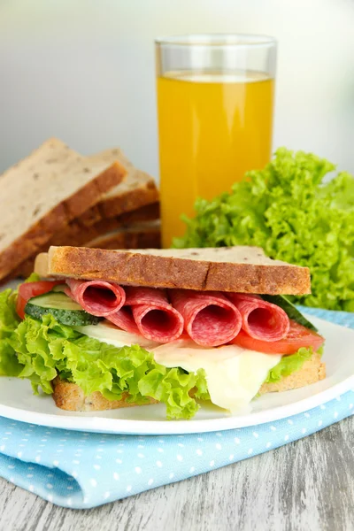 Composição com suco de frutas e sanduíche saboroso com salsicha de salame e legumes em guardanapo de cor, na mesa de madeira, no fundo brilhante — Fotografia de Stock
