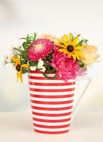 Hermoso ramo de flores brillantes en taza de color, sobre mesa de madera, sobre fondo brillante — Foto de Stock