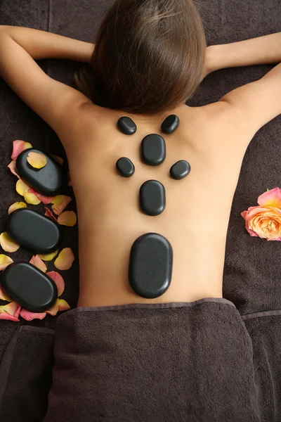 Beautiful young woman having stone massage in spa salon on color background — Stock Photo, Image