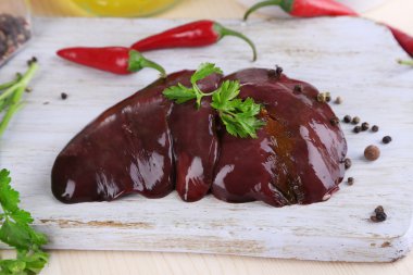 Raw liver on wooden board with spices and condiments on wooden table close-up clipart