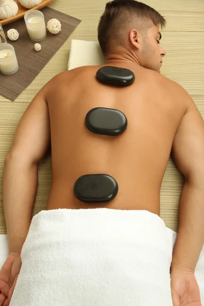 Hombre joven relajándose con piedras calientes en la espalda antes del masaje — Foto de Stock
