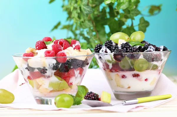 Salade de fruits dans des bols en verre, sur une table en bois, sur un fond lumineux — Photo